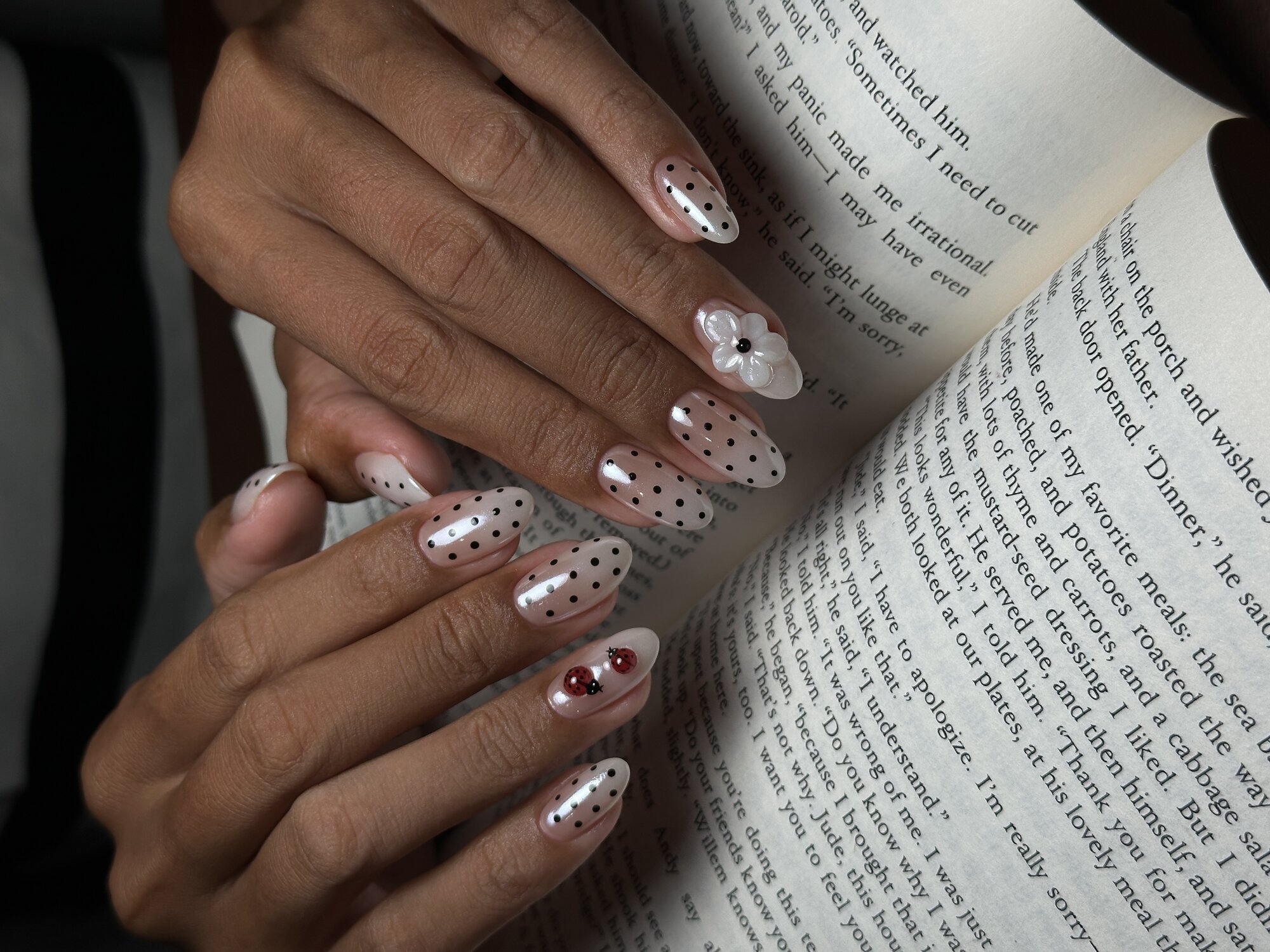 Polka-dot manicure with hand-painted three-dimensional florals and ladybird accent on an open book at Deju Studio Ubud